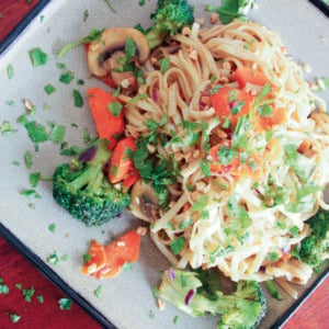 Noodles topped with vegetables and parsley on grey plate.