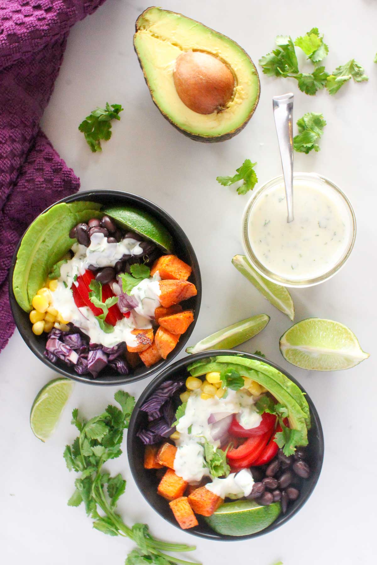 Two black bowls of sweet potato cubes, red peppers, avocados, black beans, corn, cilantro and lime