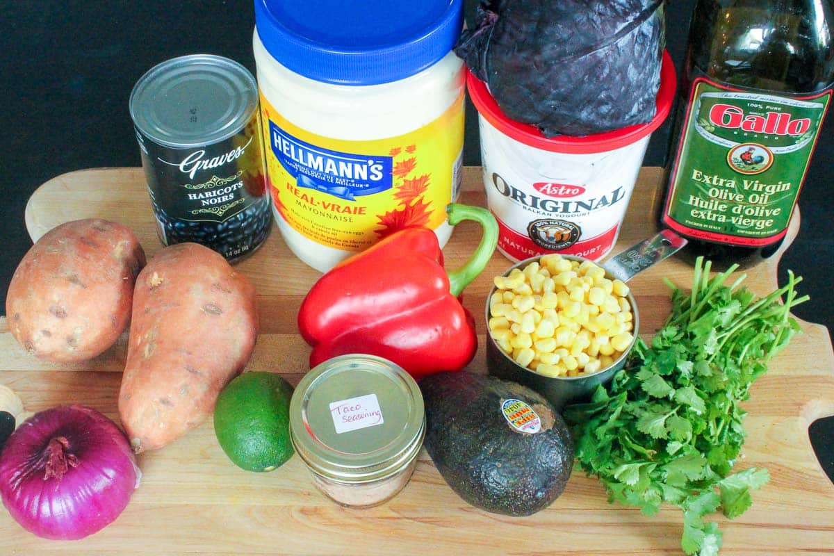 cutting board holding sweet potatoes, black beans, avocado, corn, cilantro, red onion, lime, taco seasoning, red pepper