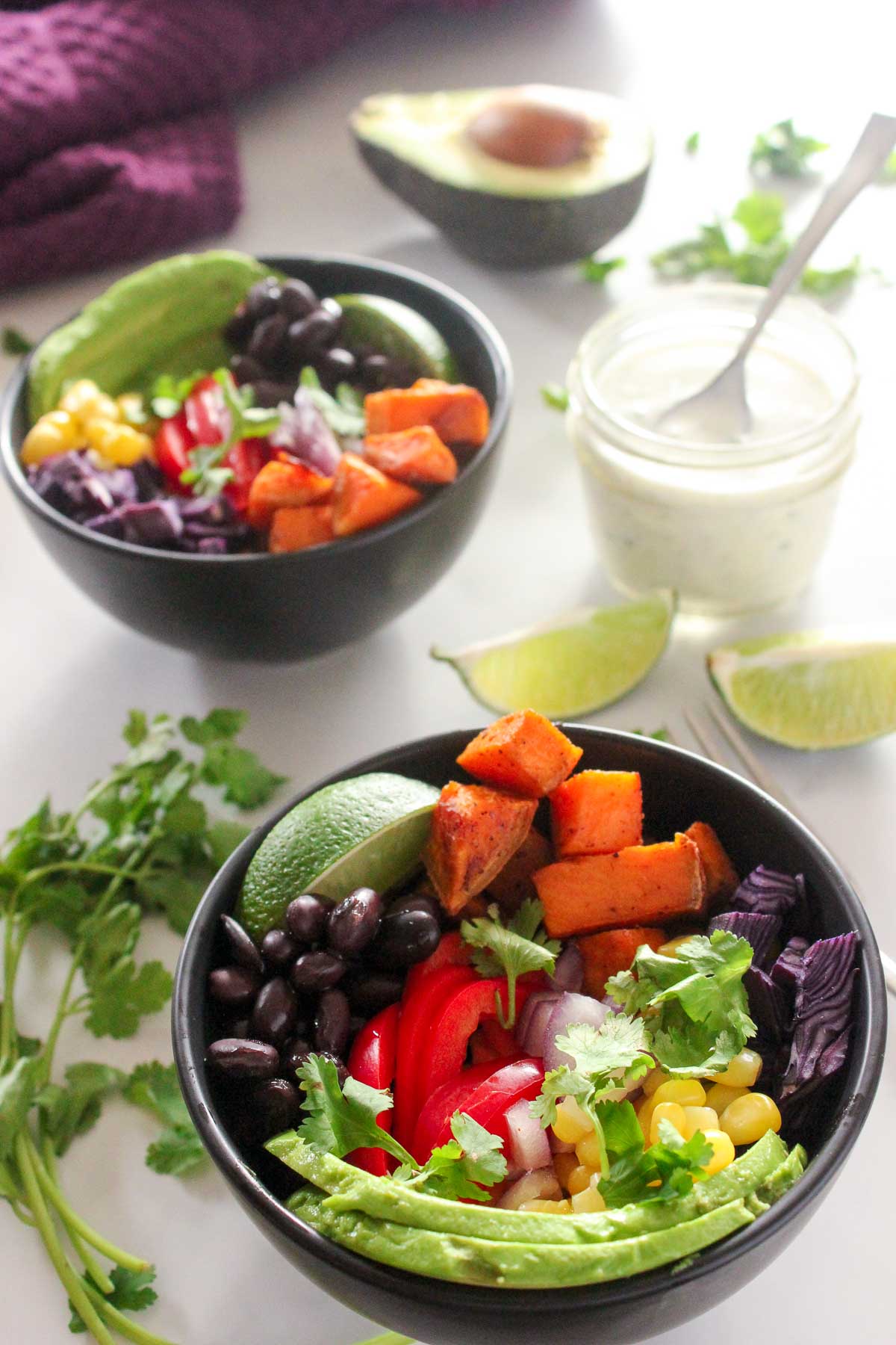 Black bowls with avocado, black beans, corn, red pepper, cilantro and sweet potatoes