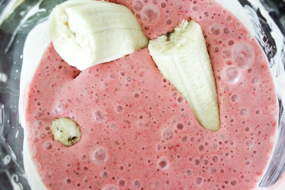 Pink smoothie in blender with bananas floating in it before mixing