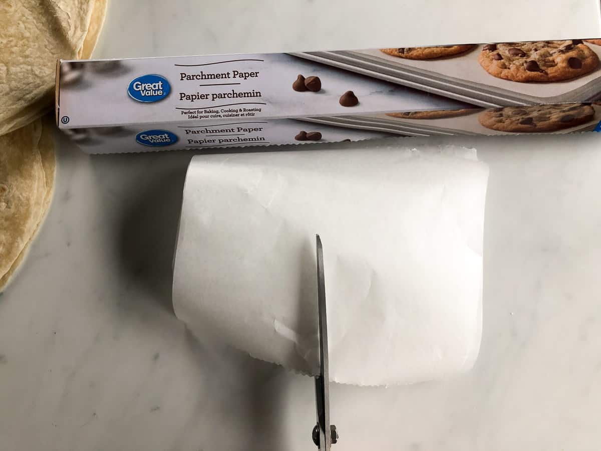 Scissors cutting parchment paper next to stack of flour tortillas