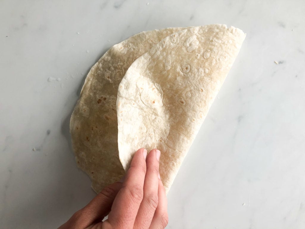 Hand folding flour tortilla wrap in half