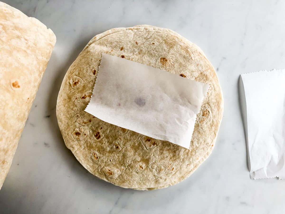 Stack of flour tortillas with a piece of parchment paper on top