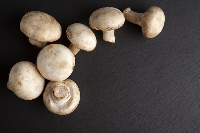 Seven clean, whole white button mushrooms on a black background.