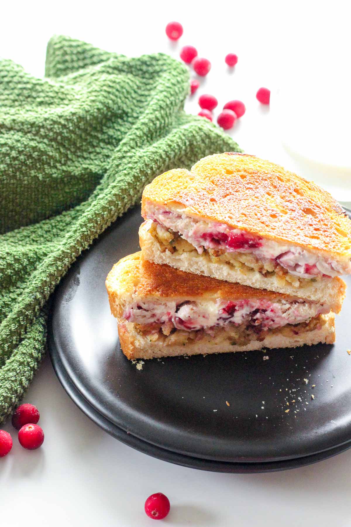 Two halves of a grilled cream cheese cranberry turkey sandwich, stacked on a black plate.