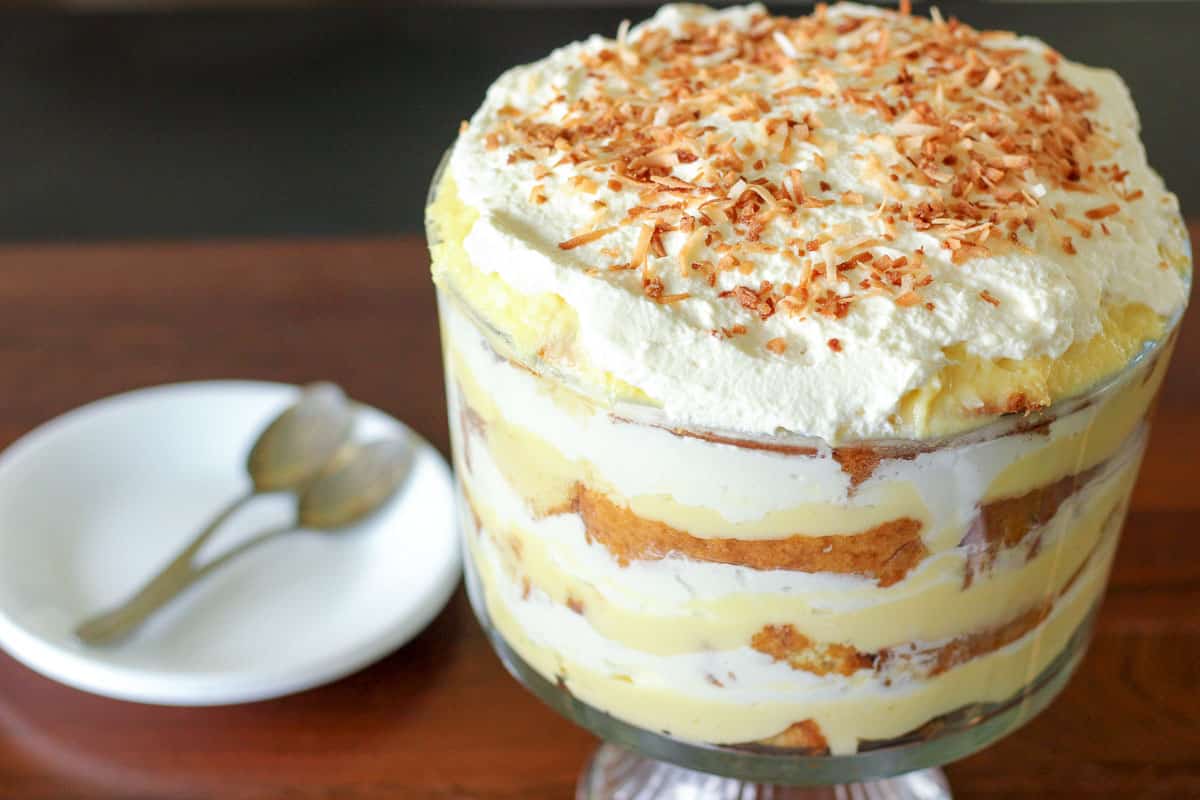 Dish of coconut cream trifle with stack of plates and spoons.