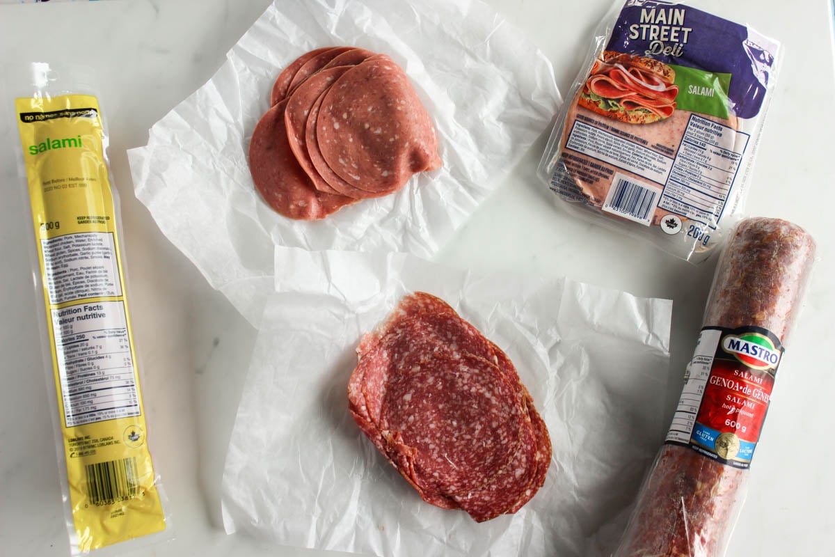 Five different types of salami on a countertop - chub, deli, prepackaged, Italian Genoa and Hungarian/German.