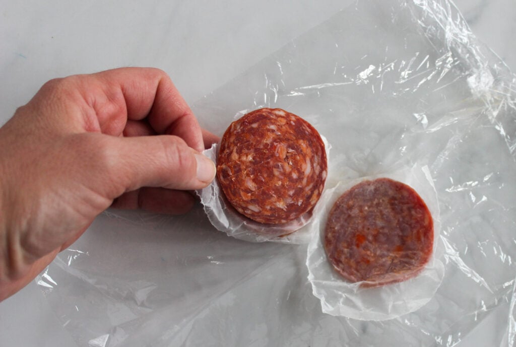A hand separating slices of Genoa salami.