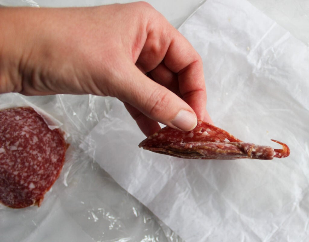 A hand separating slices of frozen Hungarian salami.