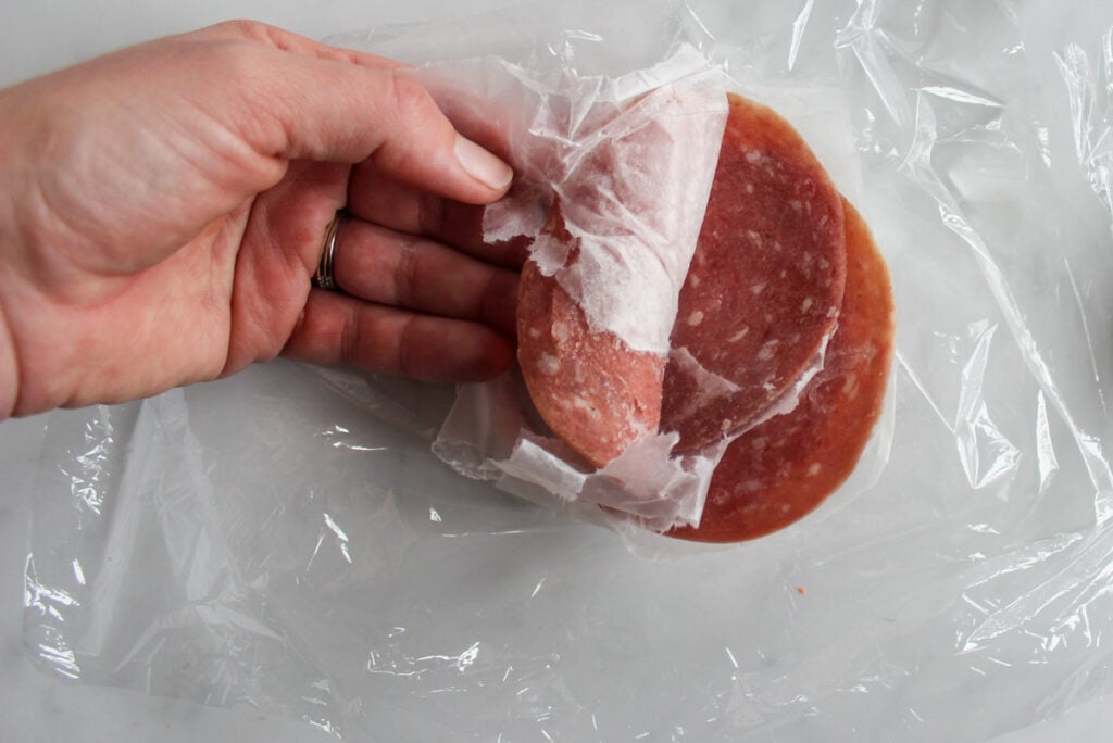 A hand separating slices of frozen deli salami.