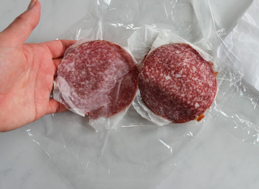 A hand separating slices of dry German salami.