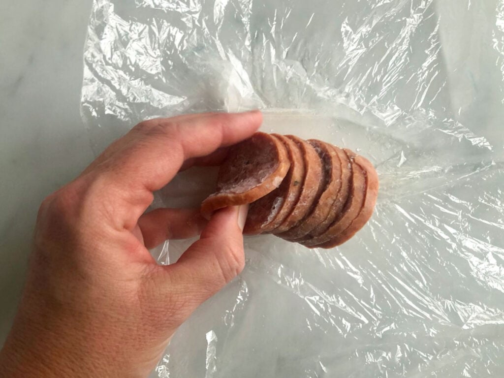 A hand separating slices of sliced salami chub.