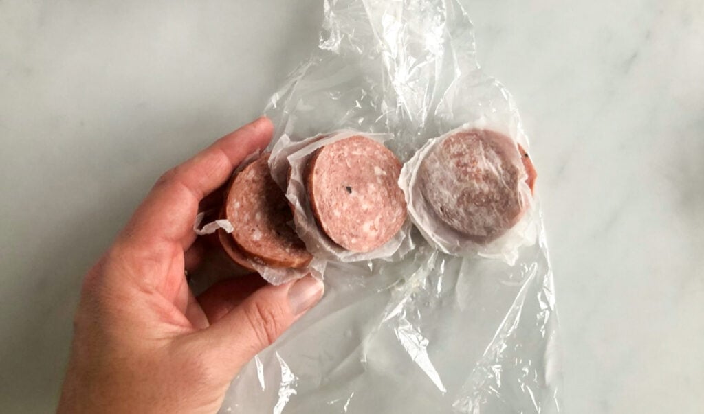 A hand separating slices of sliced chub salami.