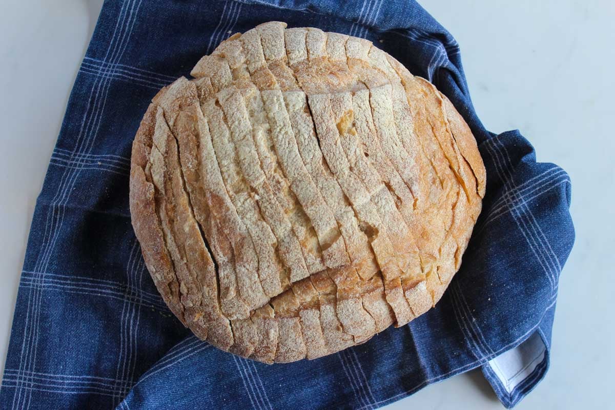 Boule of sliced sourdough bread on a blue cloth.